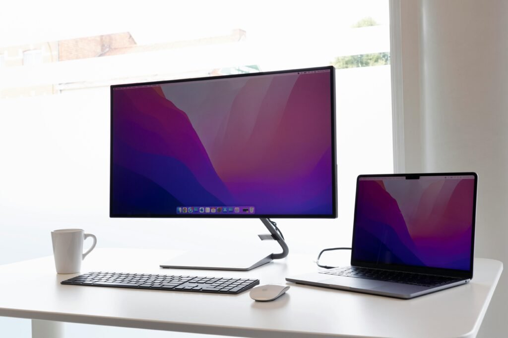 one desktop and laptop on the white table and a tea cup beside the desktop